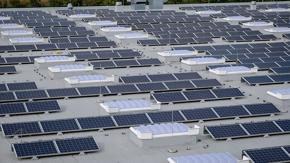 Blick auf ein Dach, auf dem neben wellenförmigen Lichtkuppeln auch Solarpanelle instaliert sind