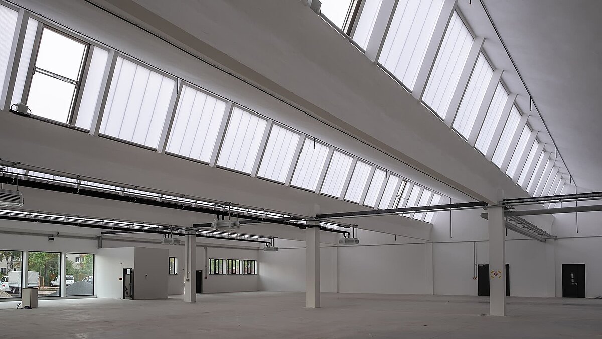 Interior view of the old post station in Leipzig, renovated with large continuous rooflights and modern white architecture.