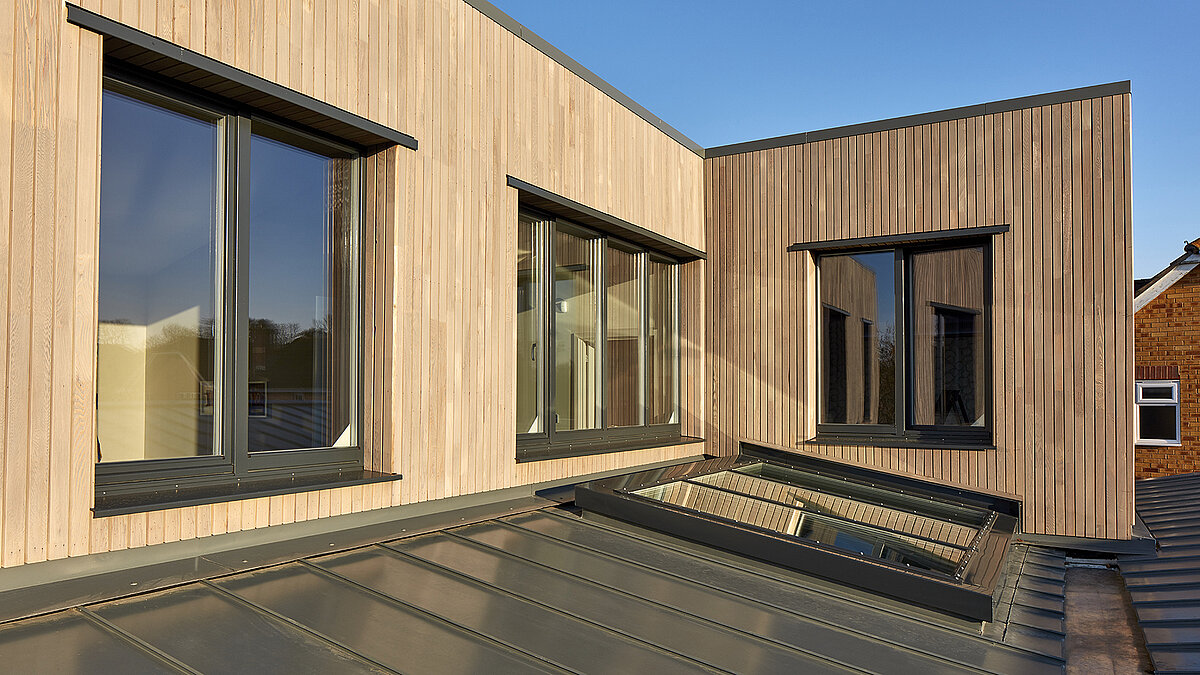 Exterior view of the modern Potton Show Homes building in England with LAMILUX PR60 glass roof, wooden façade and large windows in the warm evening light.