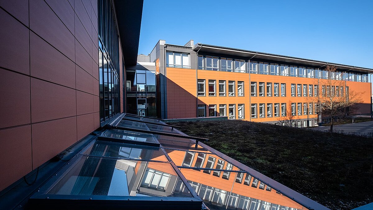 Rehau school center featuring a reflective LAMILUX PR60 glass roof and a green rooftop area in the foreground.