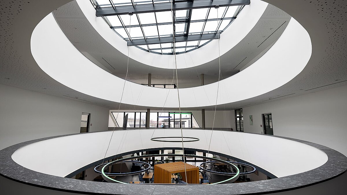 Modern atrium with oval atrium and glass roof, round LED lights and open view of the work area on the first floor.