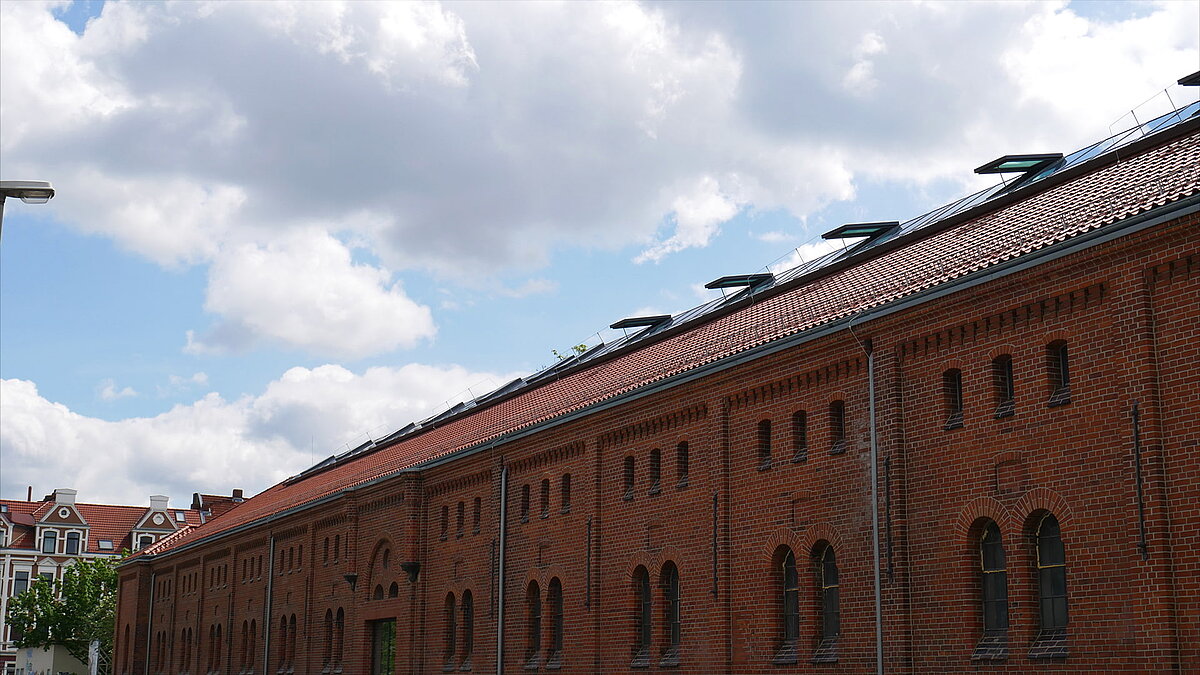 Red brick building of Leibniz University Hannover with a modern glass roof and open skylights under a cloudy sky.