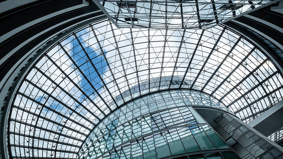 A modern, curved glass roof with a steel structure and a blue sky in a modern building