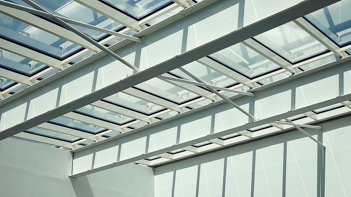 Close-up of a glass roof in Milton Park, England, featuring white steel beams and sunlight casting shadows on the walls.