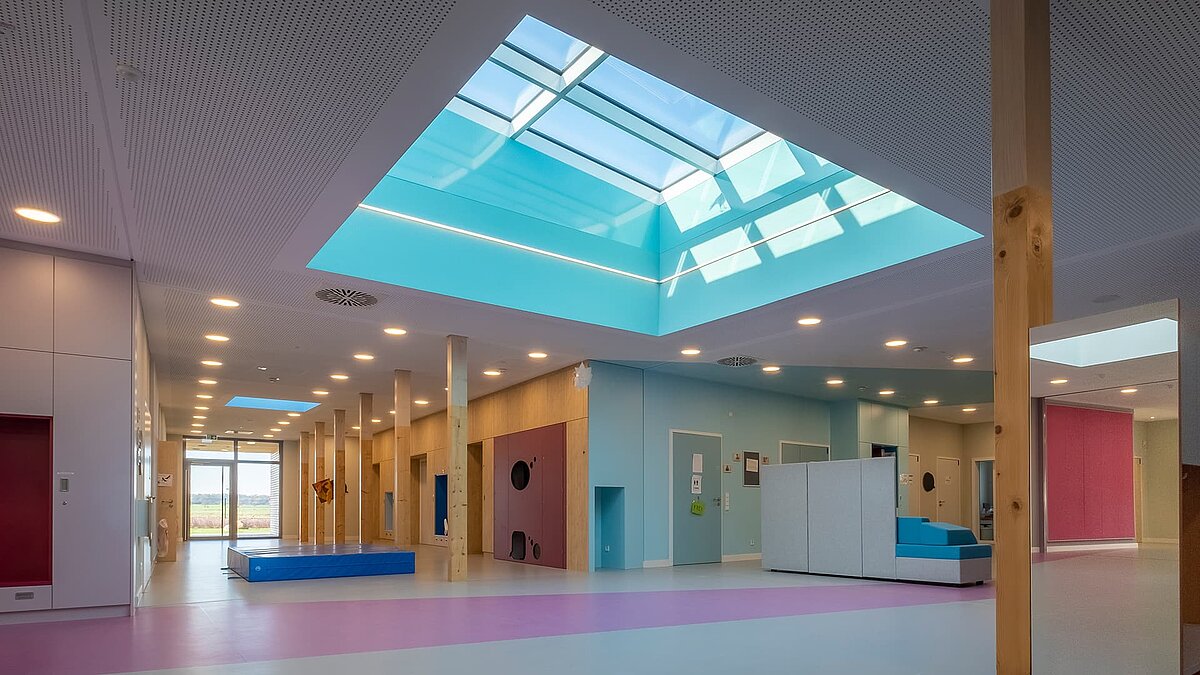 Interior view of the "World of Kids" kindergarten featuring LAMILUX flat roof window FE 3° and PR60 glass roof, creating a bright and welcoming atmosphere.