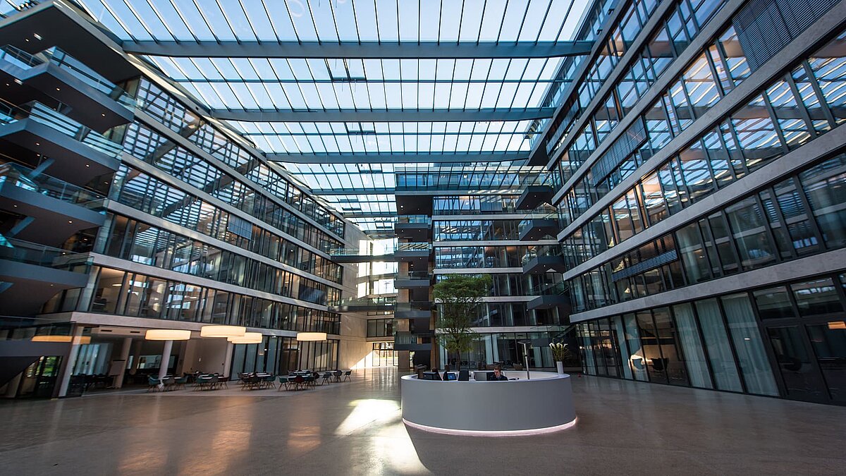 Large, modern atrium of the FGS Campus with a glass roof, sunlit spaces, central reception desk, and surrounding office floors.