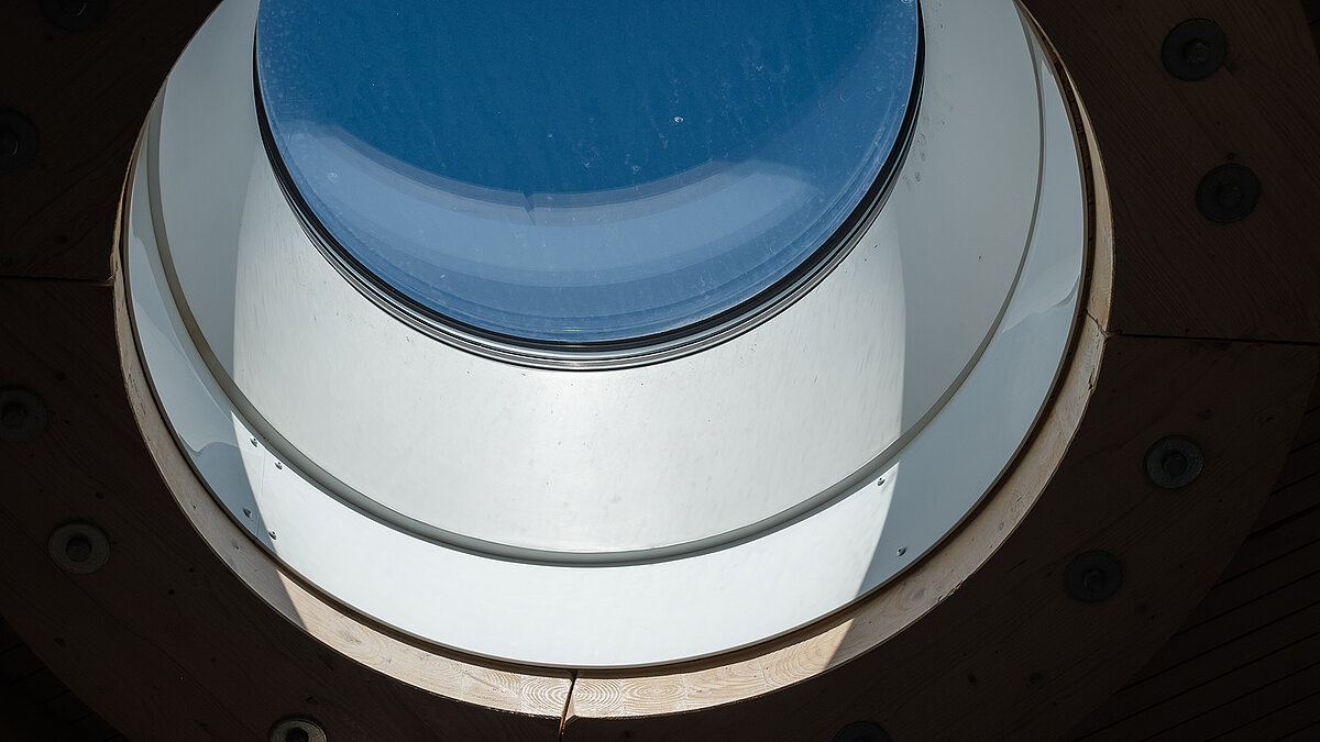 Close-up of a round skylight at the Norderney ferry terminal featuring a wooden frame and glass surface, allowing natural daylight to enter.