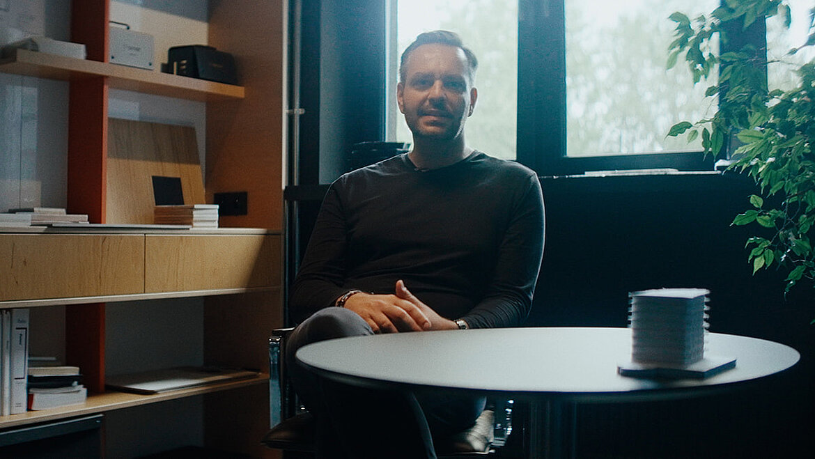 Person sitting at a table in a modern interior with shelving in the background and a cup on the table, calm and focused atmosphere