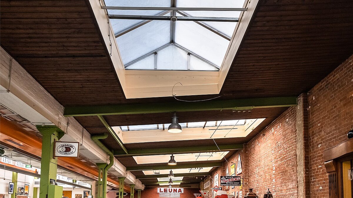 Interior view of the Zündmagnet event hall in Wurzen featuring a glass roof, green steel beams, and brick walls with industrial charm.