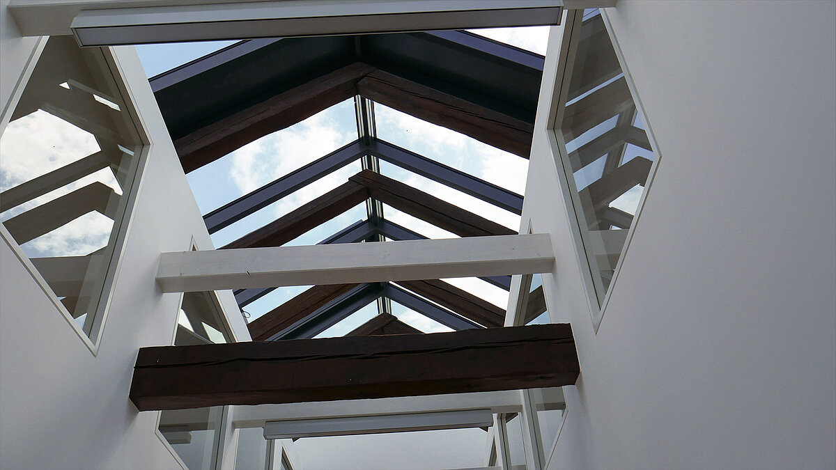 Glass roof structure with wooden beams and white steel supports at Leibniz University Hannover, view of the sky.