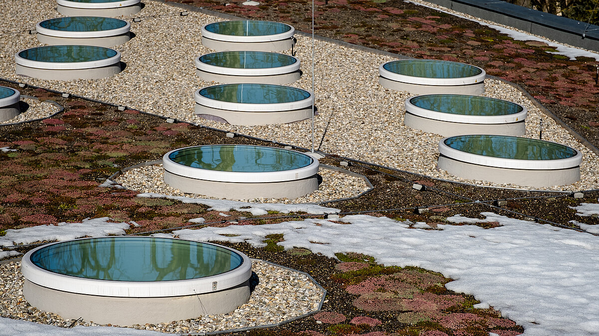 Round flat roof windows on the green roof of St. Severin Kindergarten, partially covered with snow.
