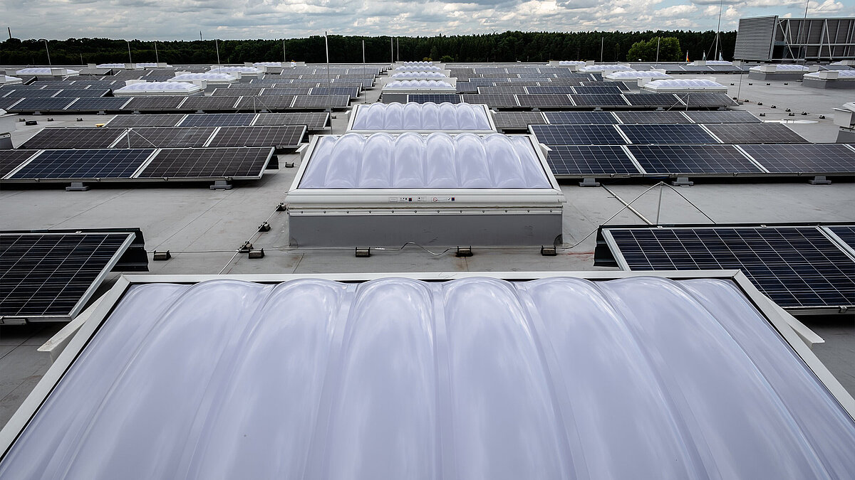 Blick über eine Reihe aus wellenförmigen Lichtkuppeln neben denen links und rechts Solarpanelle aufgebaut sind