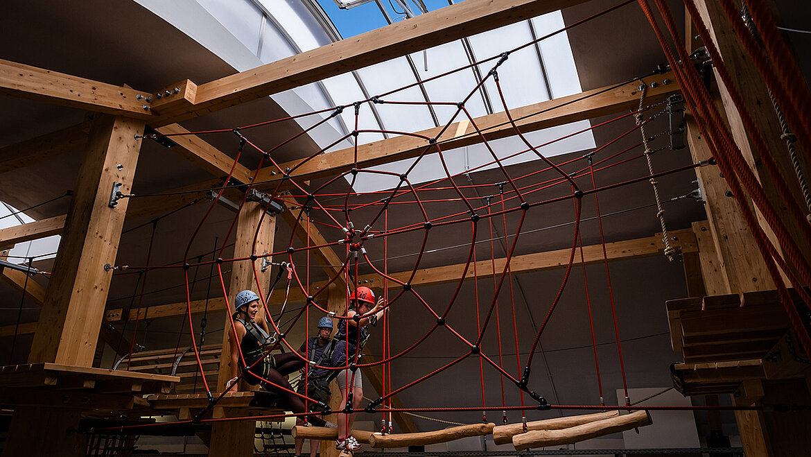 Indoor climbing course with wooden beams, red climbing net and skylight