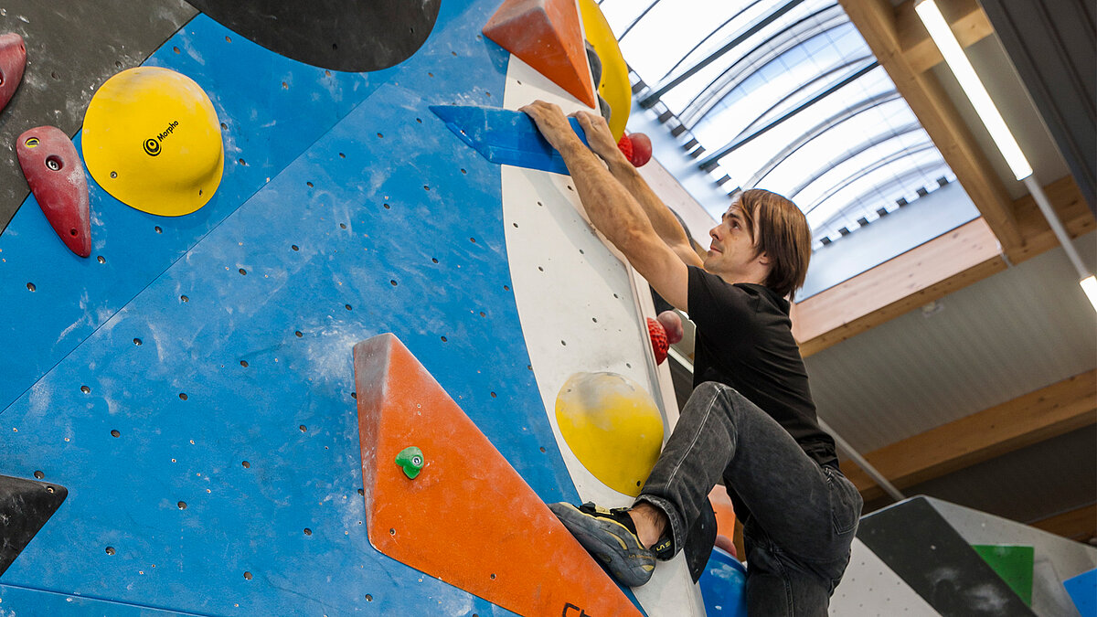 A man in black is climbing a bouldering wall in an indoor climbing centre