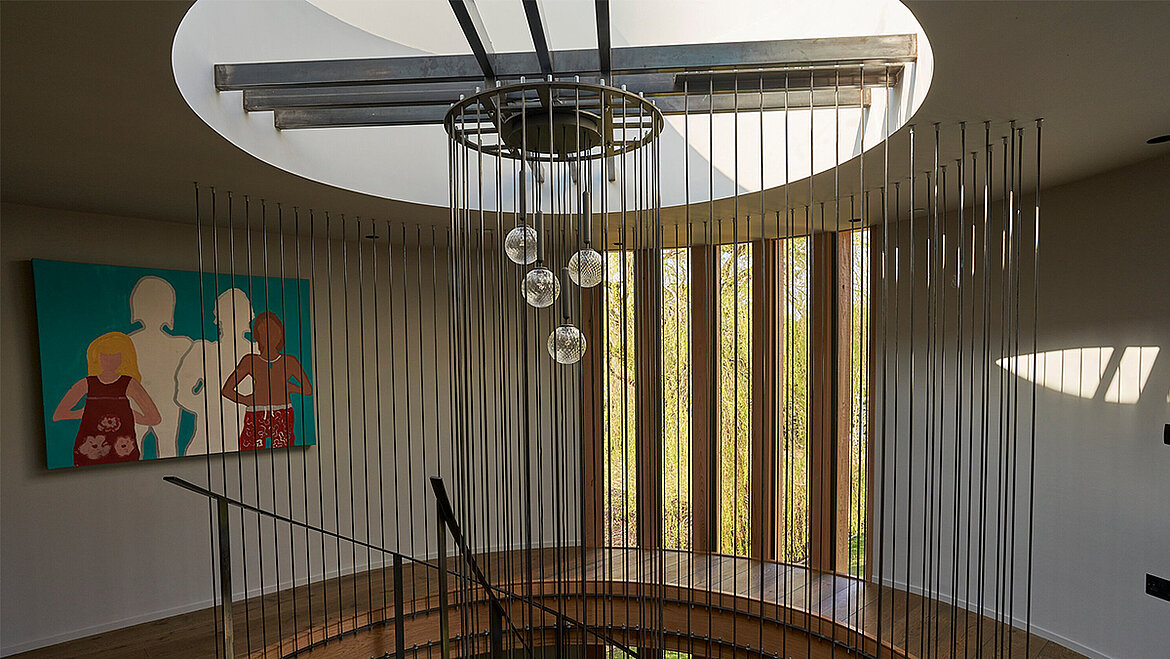 An elegant staircase with a curved wooden staircase, metal balusters, glass ball light fittings and large windows