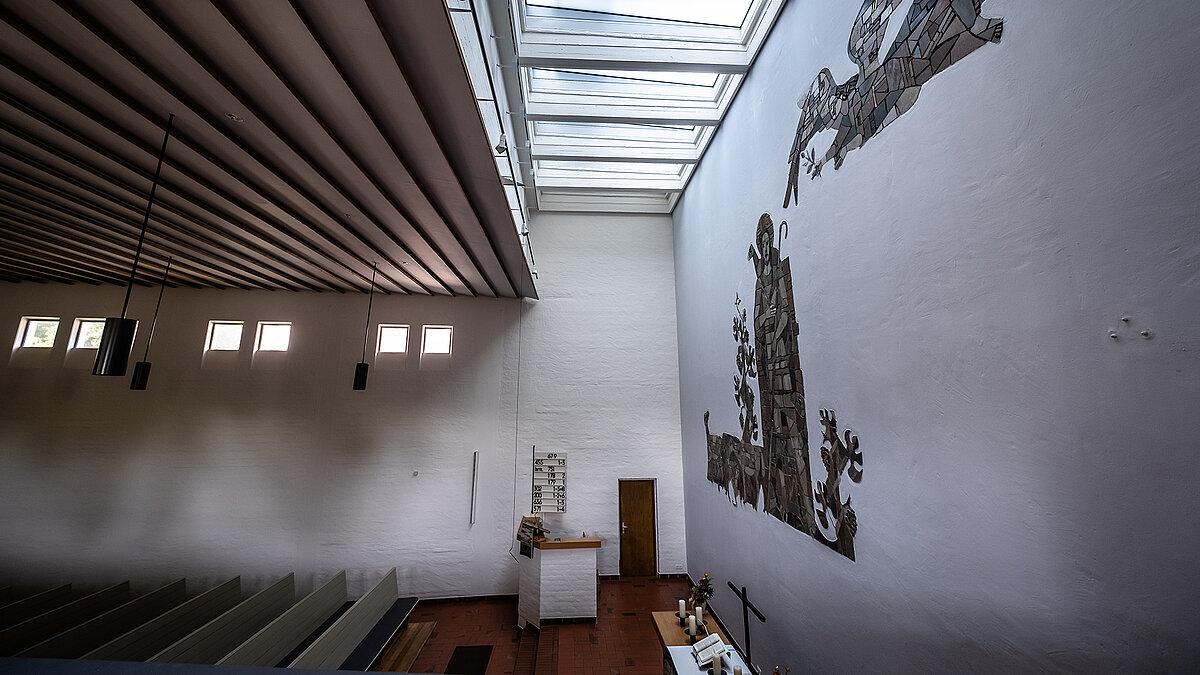 Interior of Pauluskirche in Traunreut featuring LAMILUX flat roof windows FE and a large wall mosaic depiction.