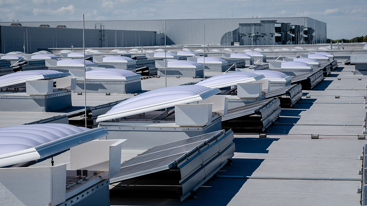 Näherer Blick auf ein Dach mit teils geöffneten Lichtkuppeln und schräg montierten Solarpanellen