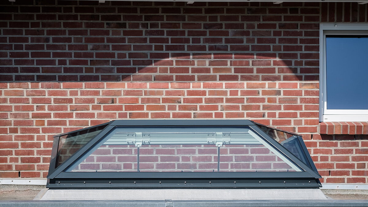 FW flat roof window by LAMILUX installed on a residential house in Hamburg, set against a red brick facade with a tiled roof.