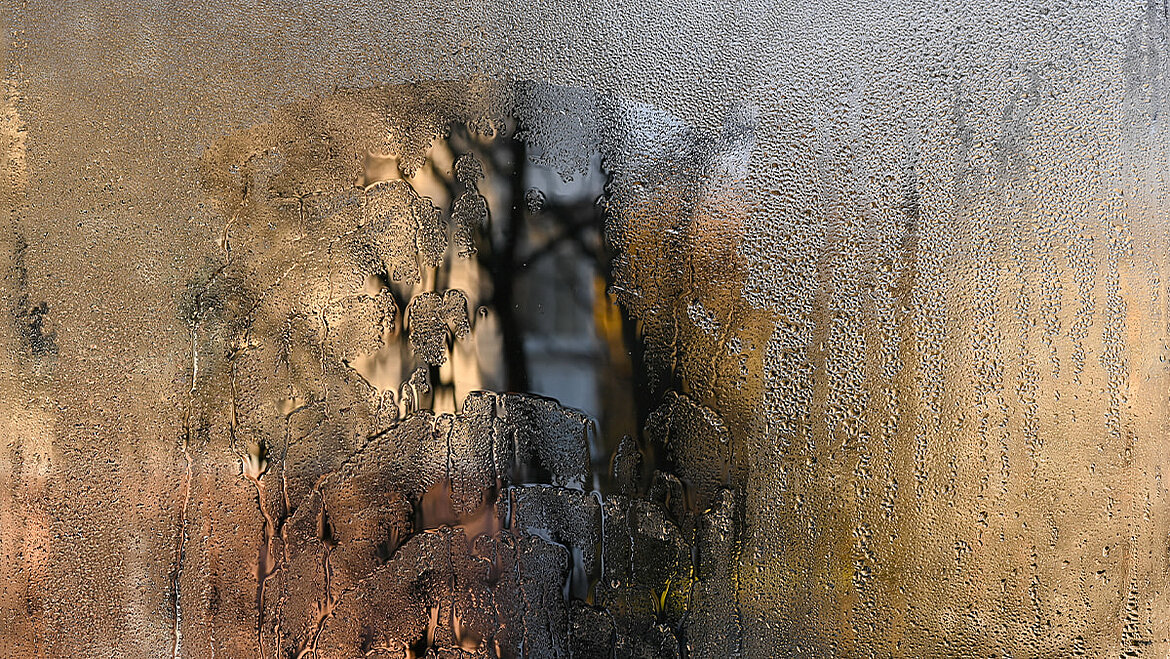 Stark beschlagene Fensterscheibe mit sichtbaren Feuchtigkeitsspuren als Zeichen von anhaltender Kondensation.