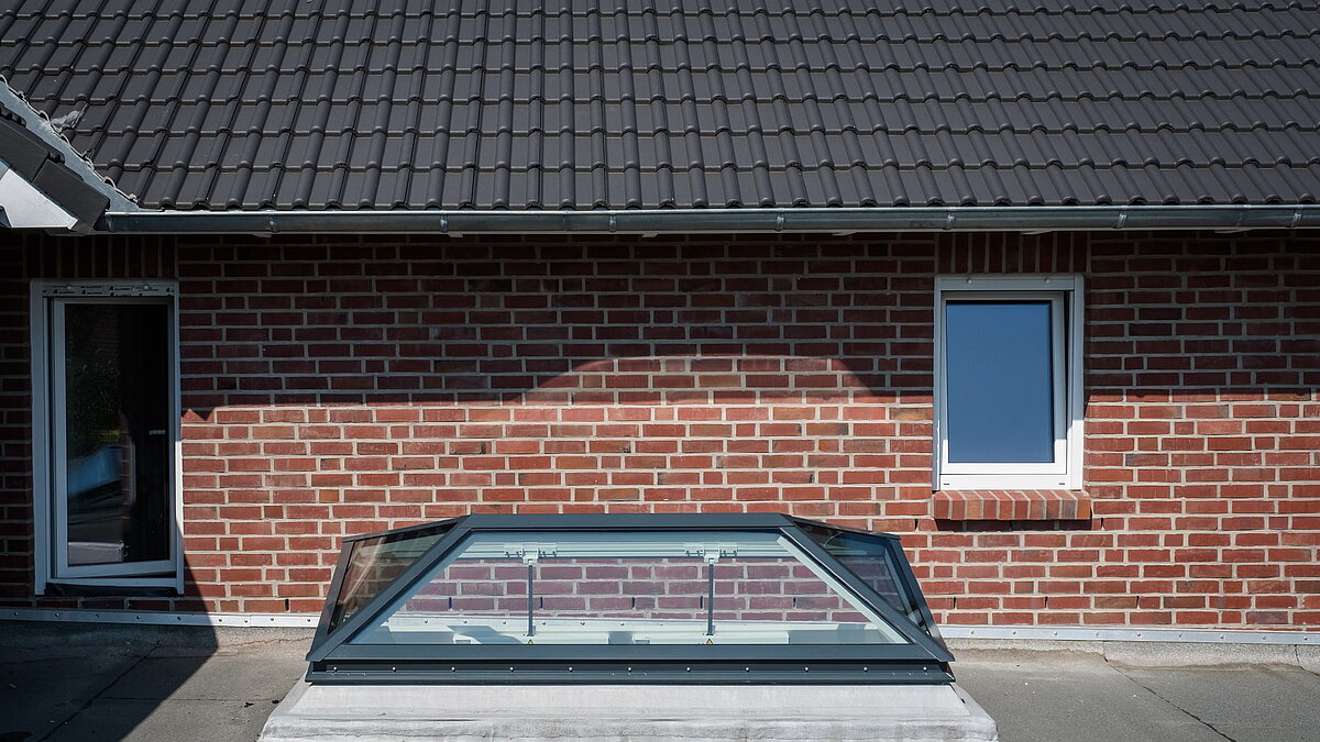 Exterior view of a residential house in Hamburg featuring a LAMILUX flat roof window FW, integrated into a red brick wall beneath a tiled roof.