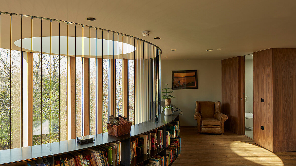 Living area with round LAMILUX flat roof window, wooden slats and built-in shelving