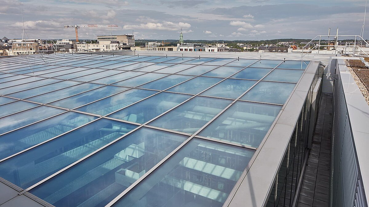Glass roof structure of the Post building in Luxembourg featuring the LAMILUX PR60 Passivhaus system, captured from the outside with sky reflections.