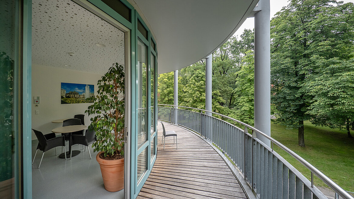 Curved balcony with a view of the countryside, adjacent to a modern office with a glass front.