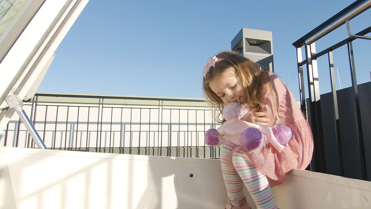 Little girl with stuffed animal sitting at an open LAMILUX flat roof access enjoying the sunshine.