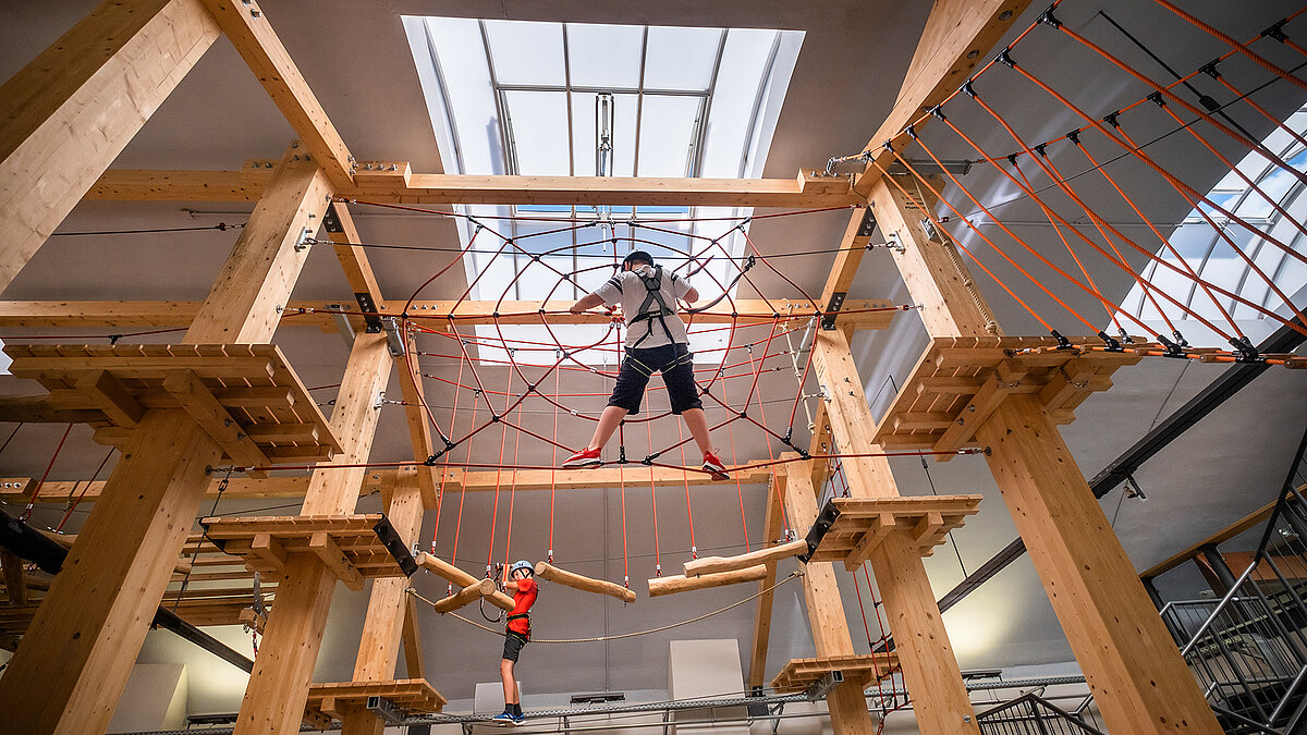 Interior view of the "Alte Brauerei" climbing hall in Eisenach featuring a LAMILUX skylight band B and two children on a high ropes course.