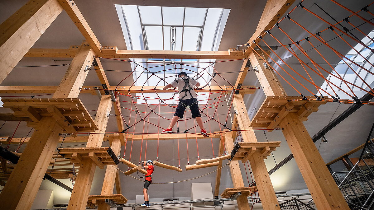 Interior view of the "Alte Brauerei" climbing hall in Eisenach featuring a LAMILUX skylight band B and two children on a high ropes course.
