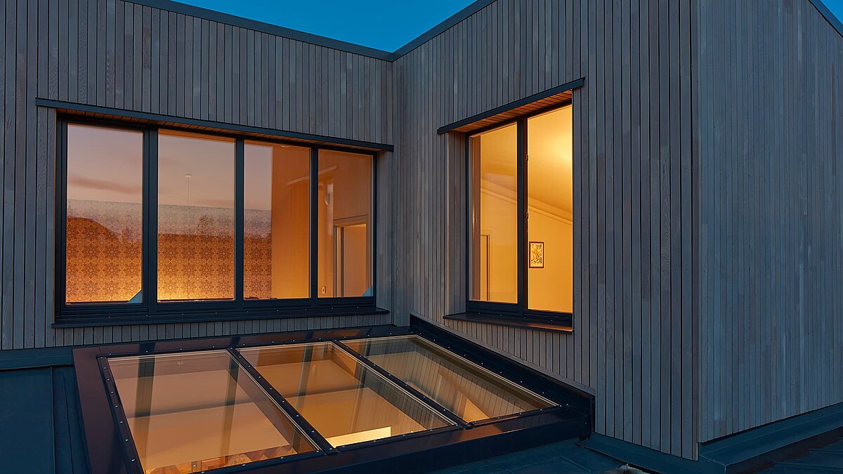 Exterior view of Potton Show Homes in England at dusk featuring a LAMILUX PR60 glass roof and illuminated interior.