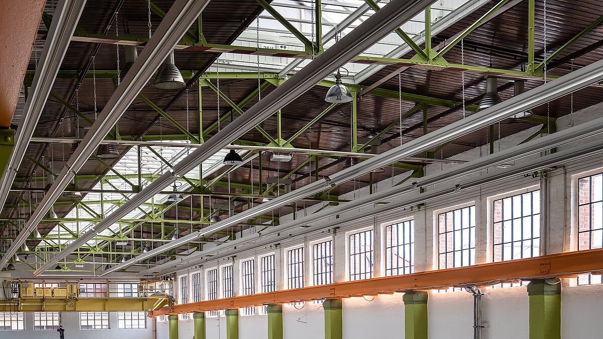 Interior view of the Zündmagnet event hall in Wurzen featuring green steel beams, a glass roof, large windows, and industrial charm.
