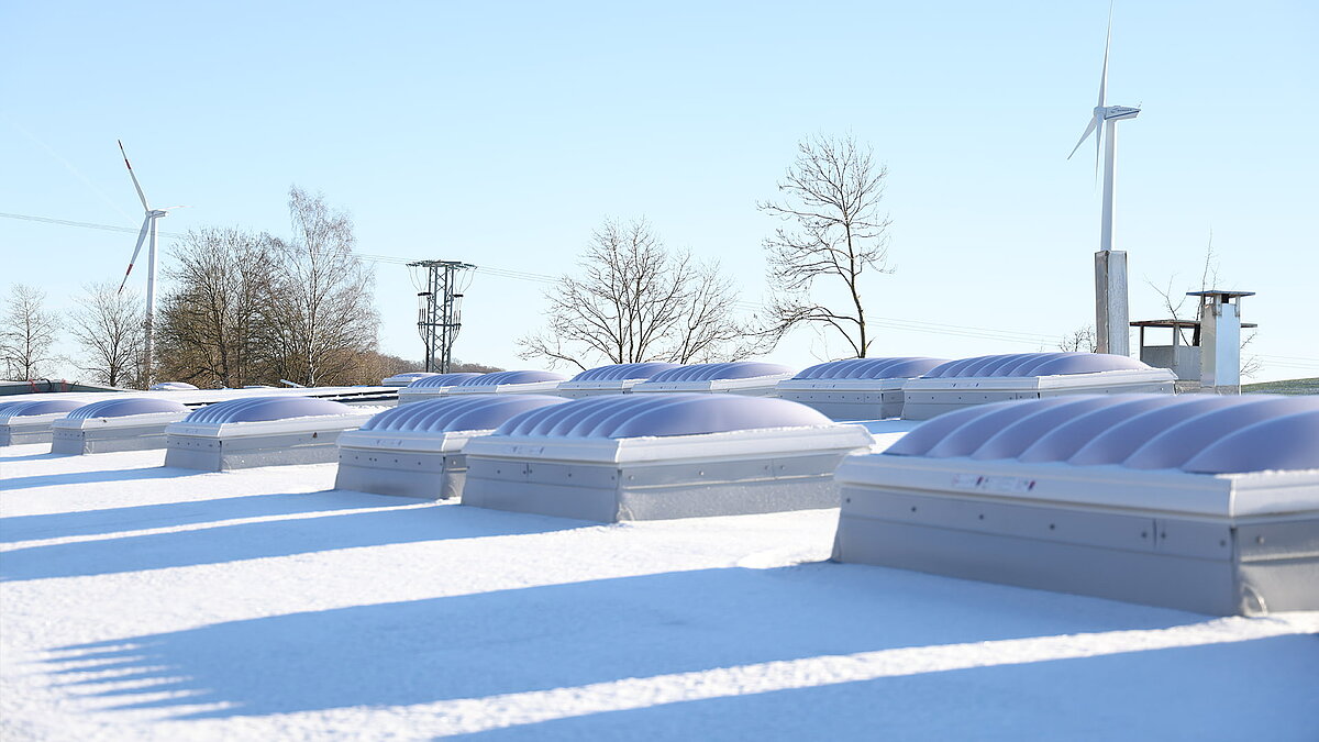 Snow-covered roof of the "Ab in die Box" building at Diemelsee with wave-shaped skylights.