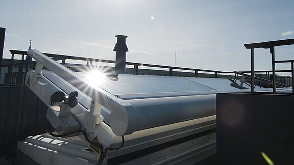 Open LAMILUX flat roof access with sunlight reflection on the glass surface.