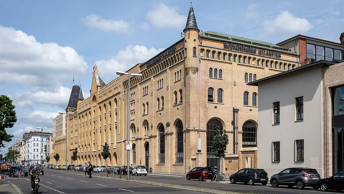 Exterior view of the Schultheiss Quartier in Berlin-Moabit, historic brick building with modern extensions, street scene with cars and cyclists.