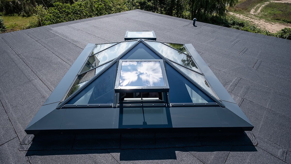 Glass pyramid on the flat roof of a single-family home in Wichmannsdorf with a reflective sky and open ventilation window.