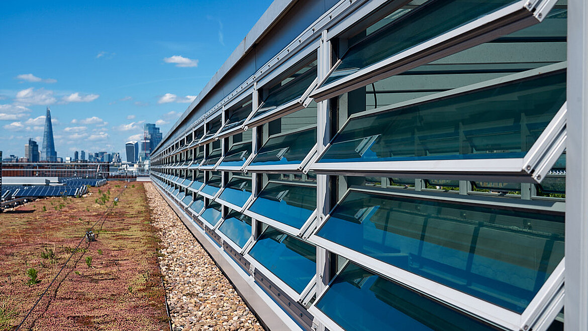 A modern building with openable glass louvre windows, a green extensive roof and a strip of gravel