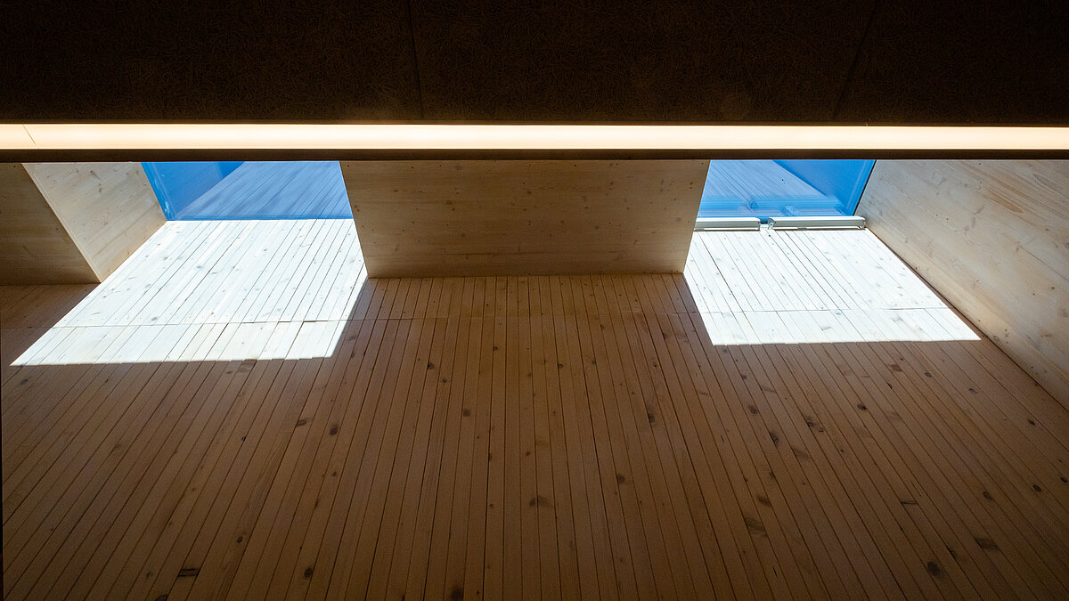 Interior of the Waltenhofen daycare center with natural daylight through skylights, wooden walls, and shadow patterns.