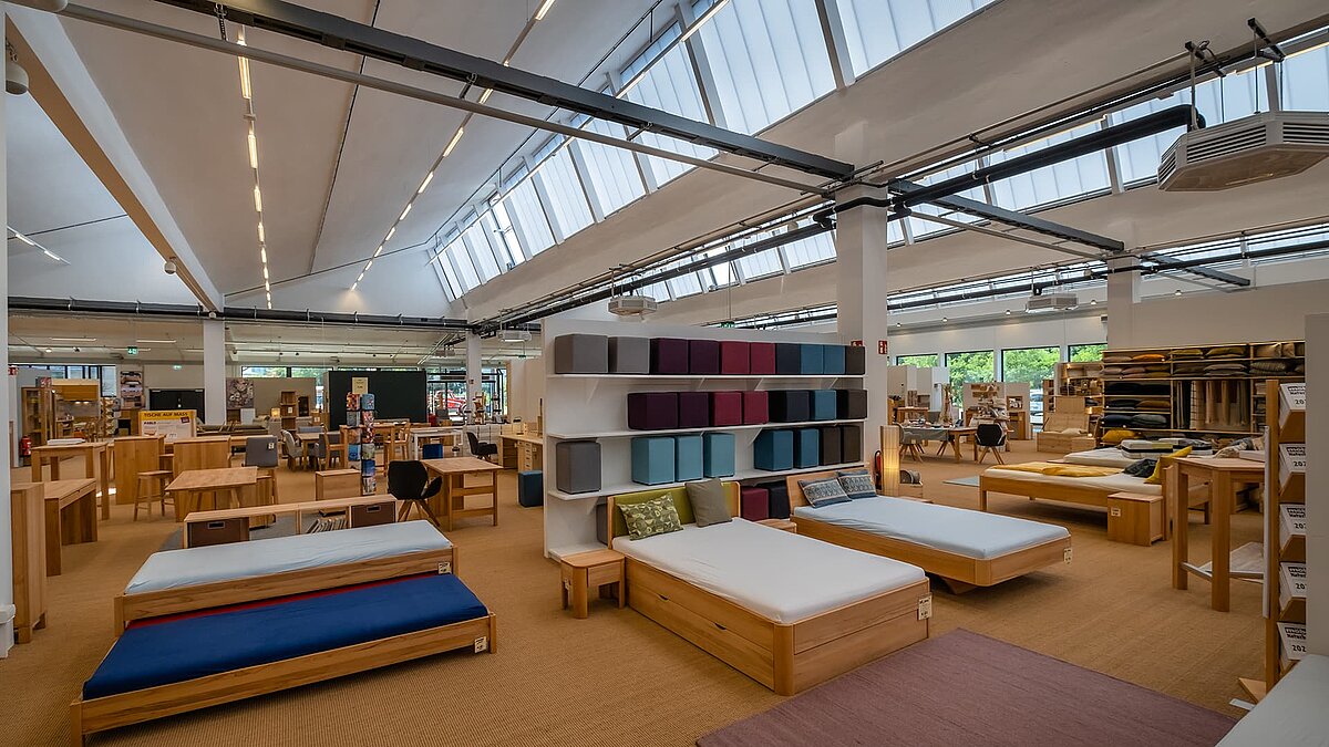 Interior view of the old post station in Leipzig, with natural light from continuous rooflights and modern display of beds and shelves.