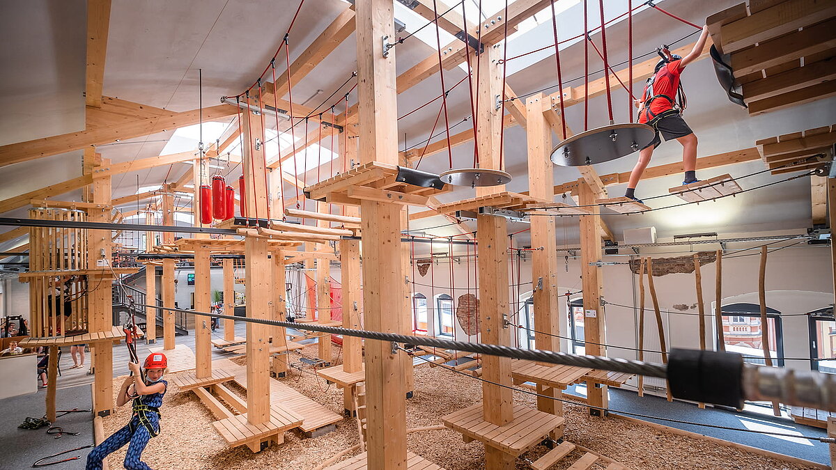 Indoor climbing park with wooden structure, rope elements, and secured participants.