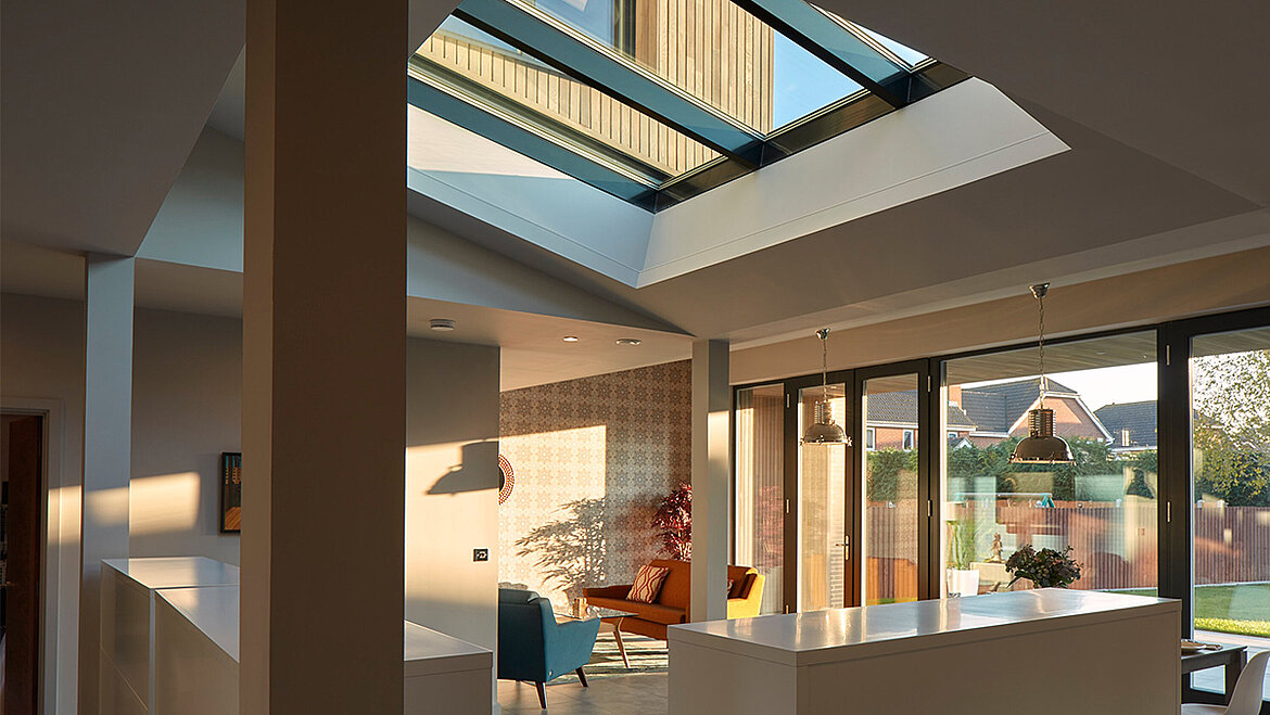 Open-plan kitchen and living room with large roof lantern skylight, white island, mid-century furniture and garden bifold doors