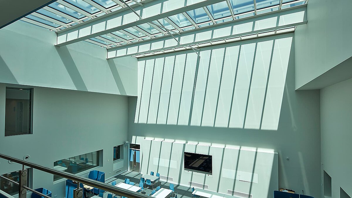 Interior view of a modern building in Milton Park, England, featuring a large glass roof casting sunlight onto the white walls of the atrium.