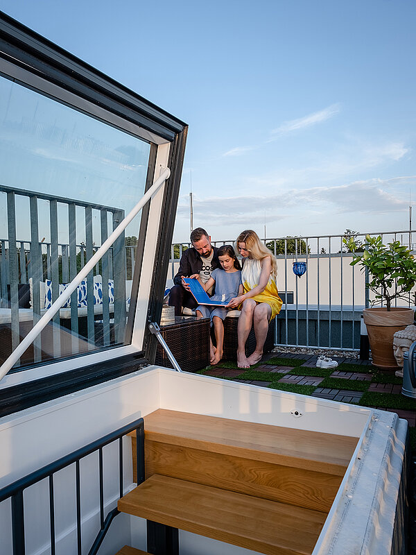 Family sitting on the rooftop terrace of a townhouse in Berlin, next to an open flat roof access.