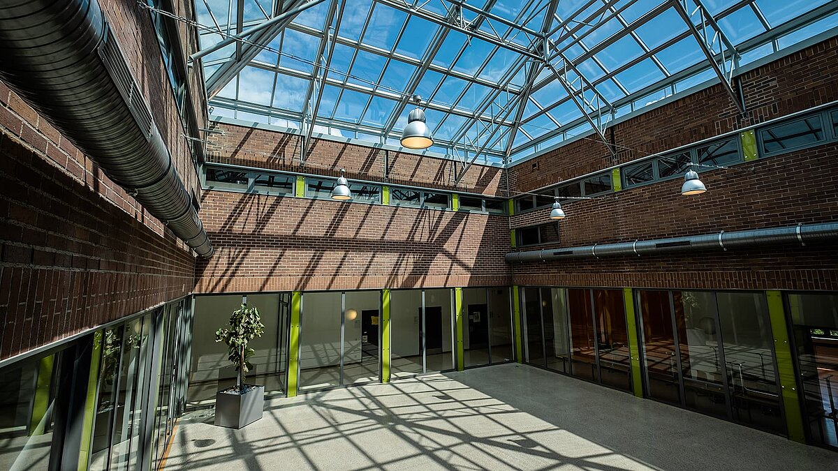 Interior view of the Dante-Gymnasium featuring a large glass roof, steel structure, brick walls, and natural light flooding the space.