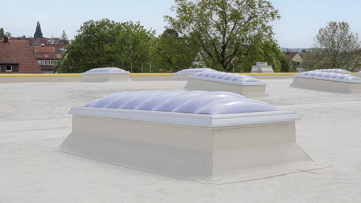 Flat roof with multiple plastic skylights in front of residential area and trees