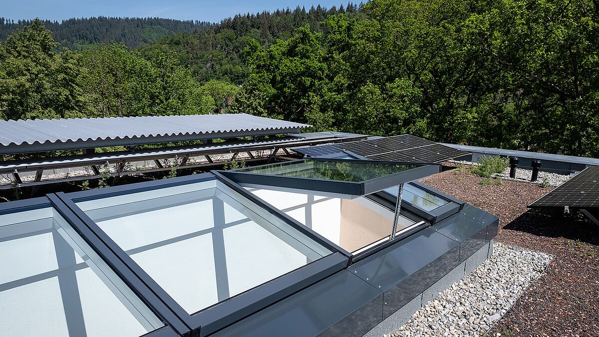 Residential building in Freiburg with a modular glass roof by LAMILUX, partially opened, surrounded by solar panels and a green flat roof.