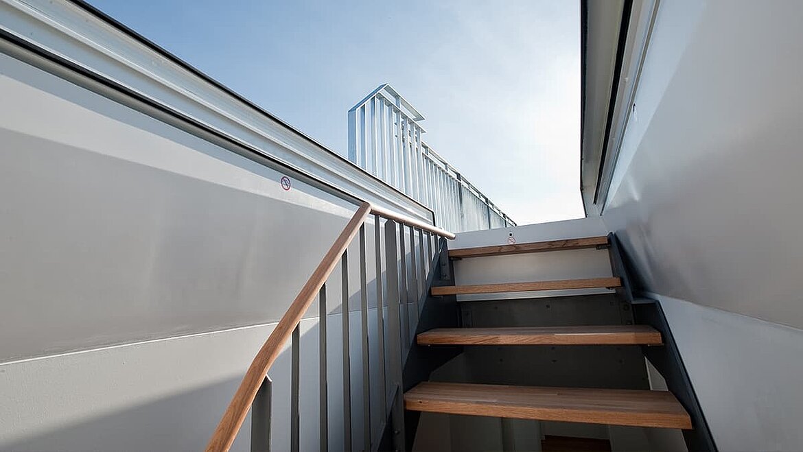 Modern staircase with glass railings leading to a rooftop terrace.