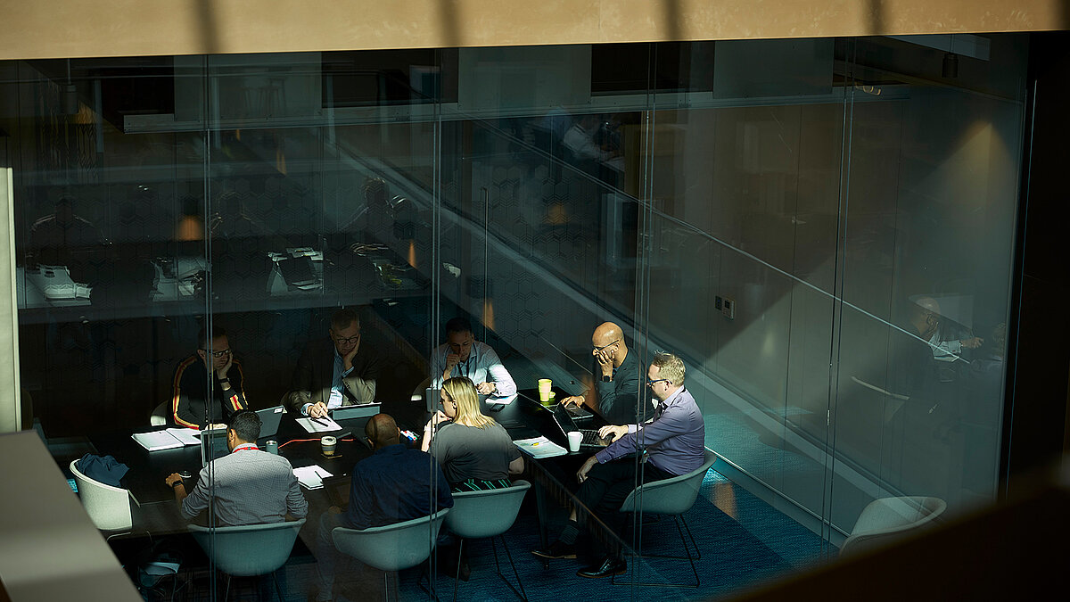 Conference room with meeting table and people behind large glass facade