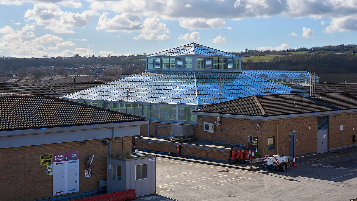 Large, curved glass roof with blue structure on a flat roof in an industrial environment, daylight