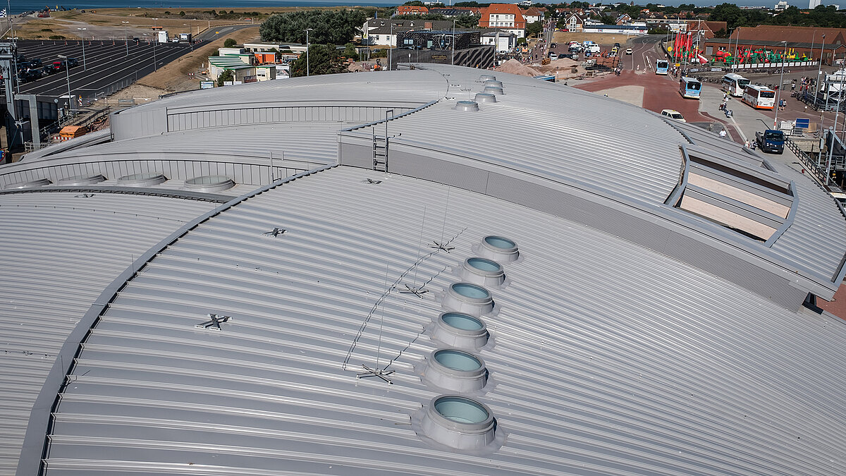 Roof of the Norderney harbour terminal with round flat roof windows and undulating metal construction.
